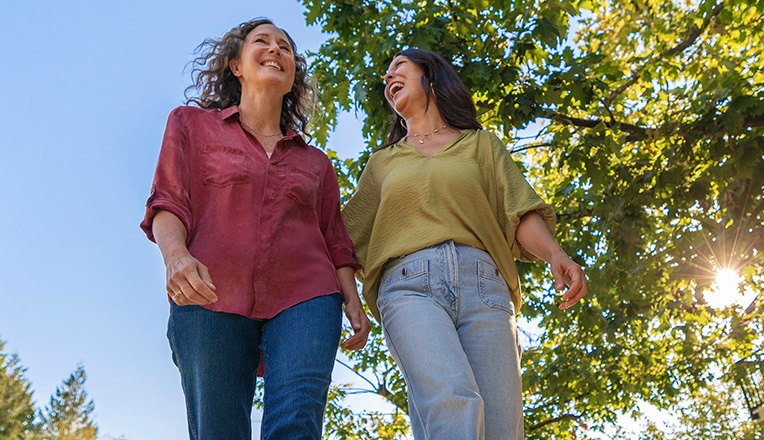 Two smiling women walking outdoors under a tree