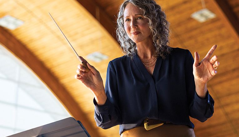 Woman holding a baton while conducting musicians